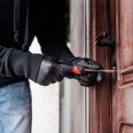 Cropped view of housebreaker in leather gloves breaking door lock with screwdriver