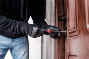 Cropped view of housebreaker in leather gloves breaking door lock with screwdriver